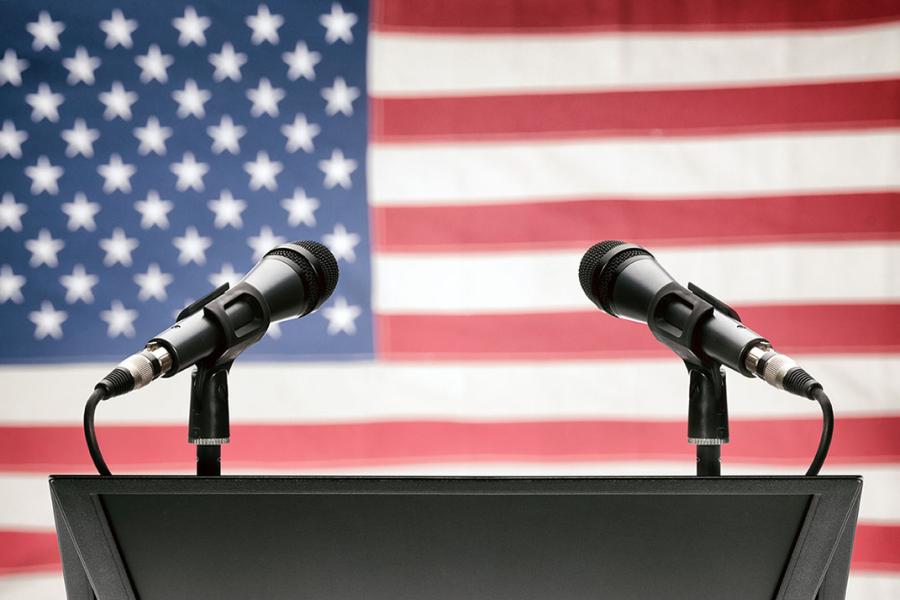 Image of lectern with two microphones with American flag in background