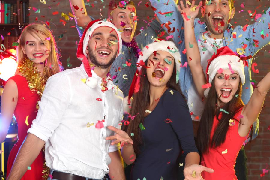 A group of people celebrate and throw confetti while wearing Santa hats.