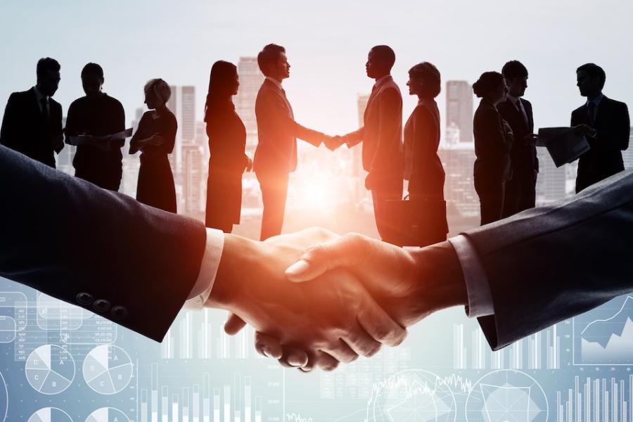 Two teams of corporate business executives shake hands while an enlarged handshake is superimposed in front of them.