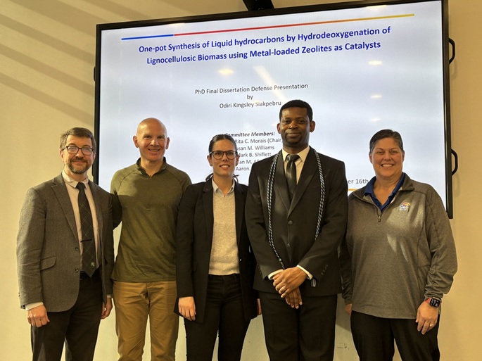 Kingsley stands in front of his presentation with his committee members