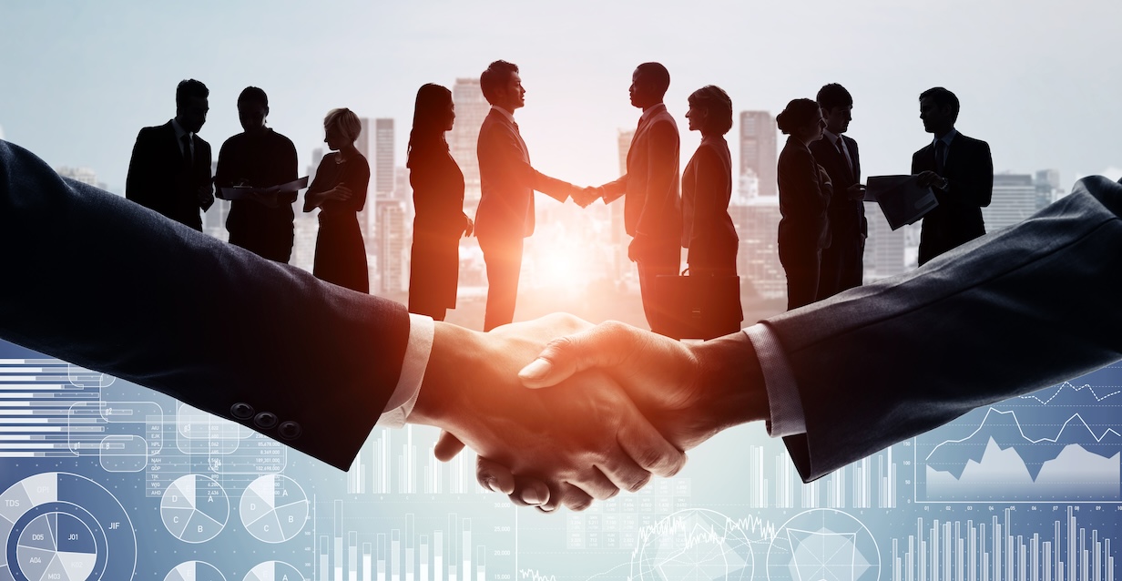 Two teams of corporate business executives shake hands while an enlarged handshake is superimposed in front of them.