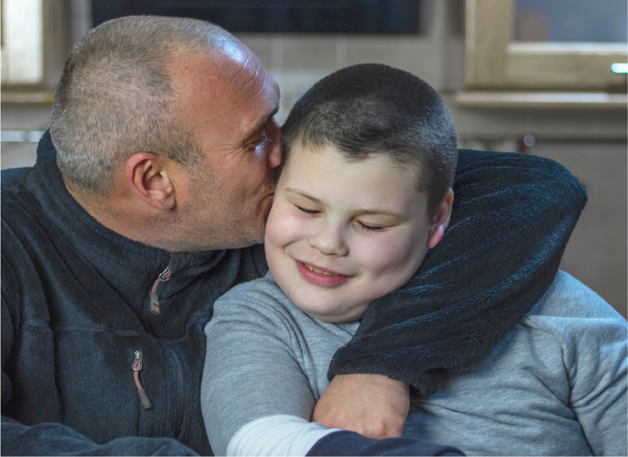 A father hugs his school-aged son who is smiling while they sit together