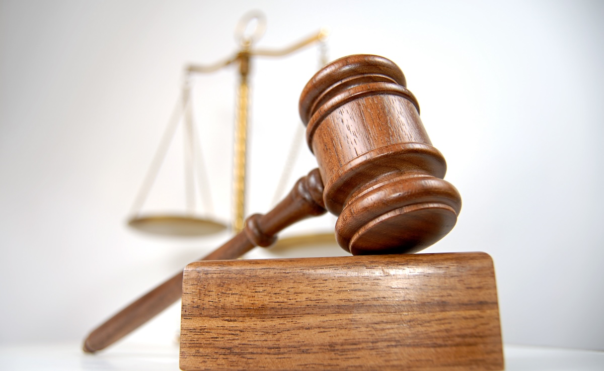 A gavel sits on a sound block while the scales of justice loom in the background.