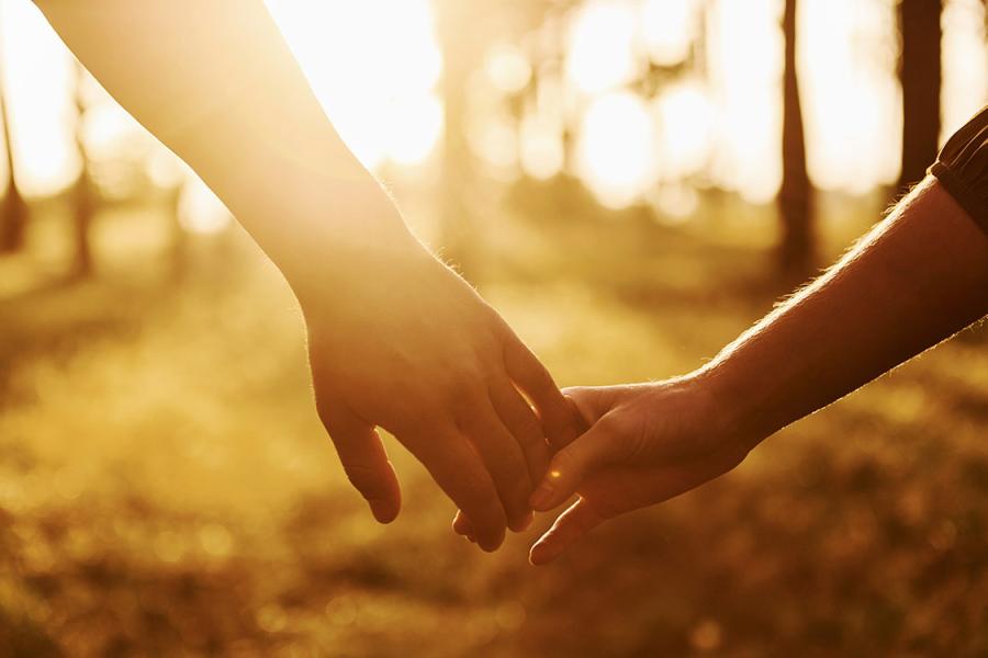 Two people holding hands while a bright sun shines in the background, creating a glow on the image.