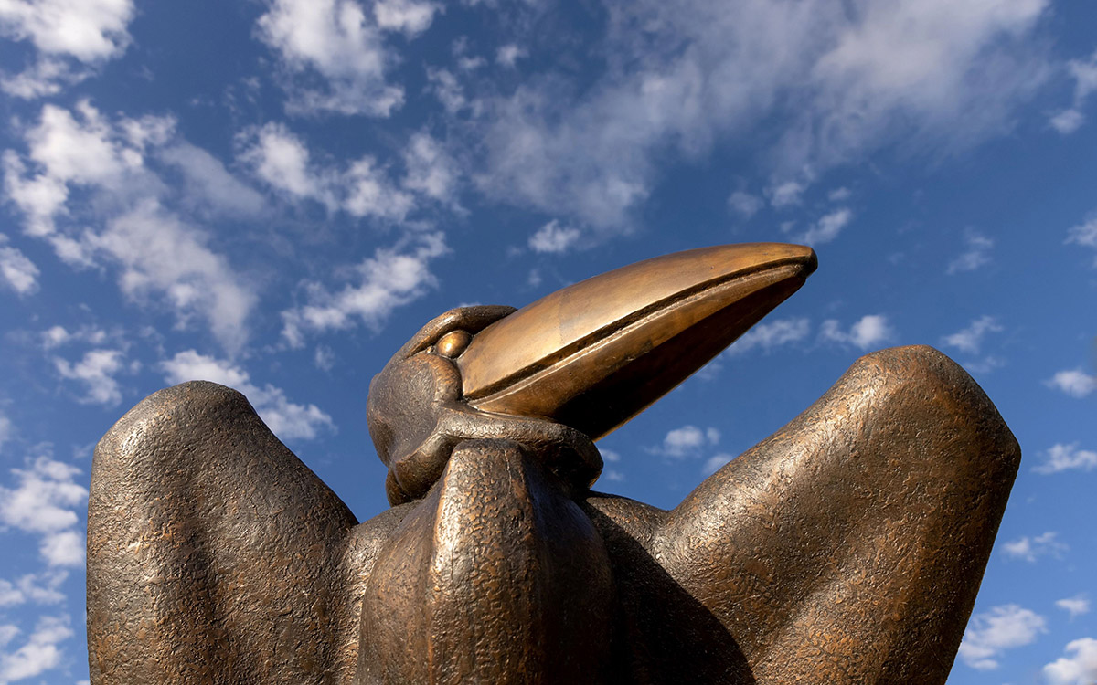 A close-up view of a bronze Jayhawk statue with a cloudy sky in the background.