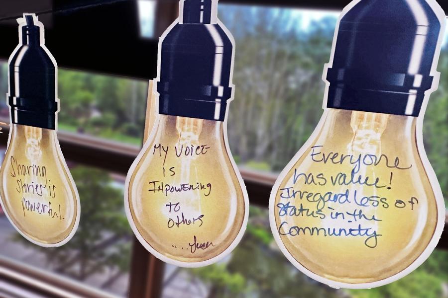Pieces of paper in the shape of lightbulbs with messages written on them in pen. Sharing stories is powerful. My voice is empowering to others. Everyone has value. Regardless of status in the community.