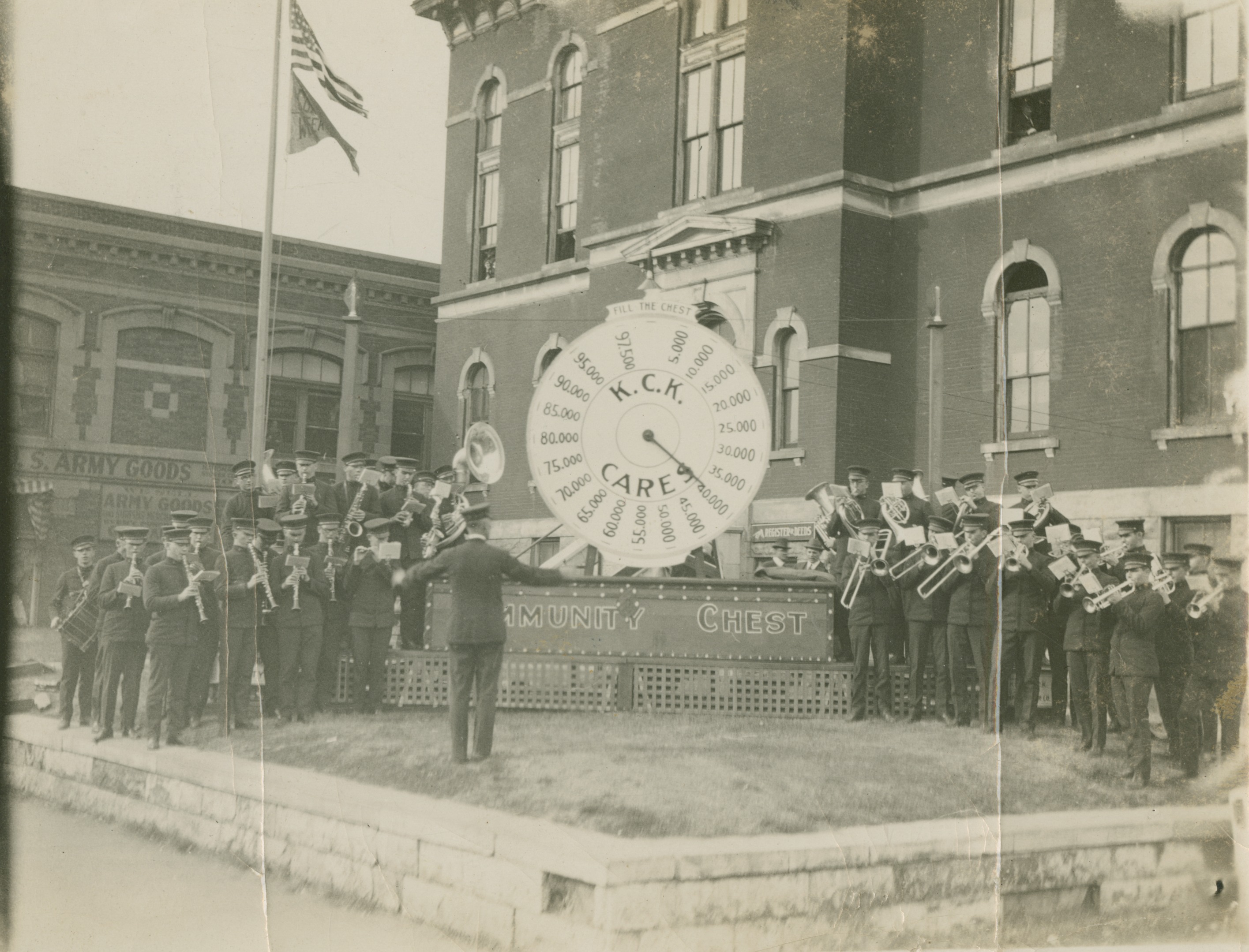 A black and white photo of the KU Marching Band standing in front of a building, centered around a giant promotional clock.