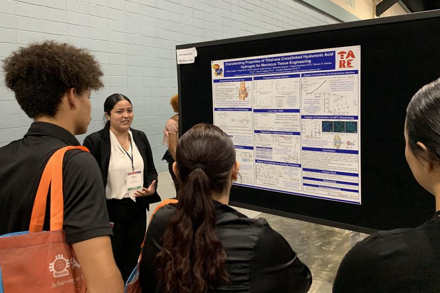 KU student Kayla Castillo gives a research presentation standing next to posterboard.