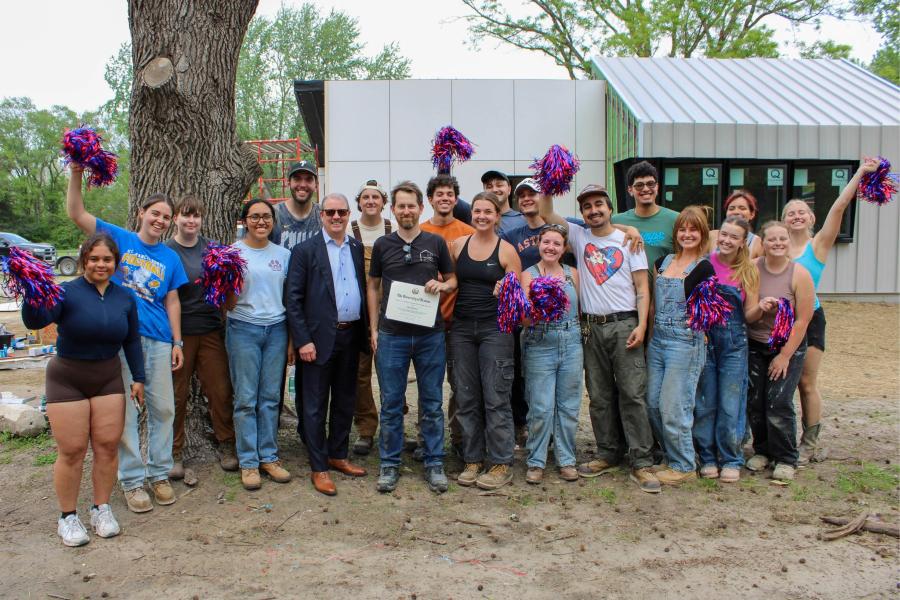 Professor Chad Kraus poses with Kemper fellowship certificate alongside Chancellor Girod and class in front of construction project