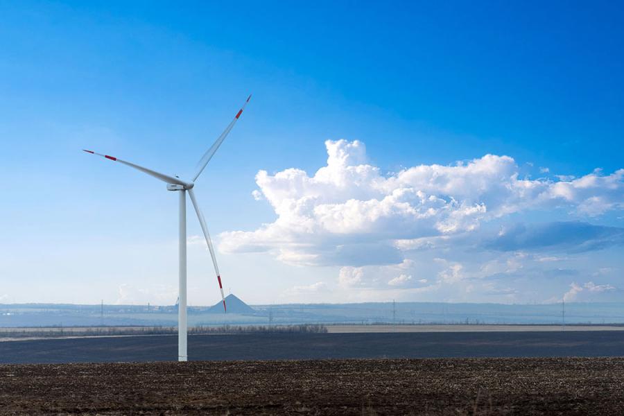 A wind turbine set against a blue sky, with a coal mine waste rock pile visible in the background.