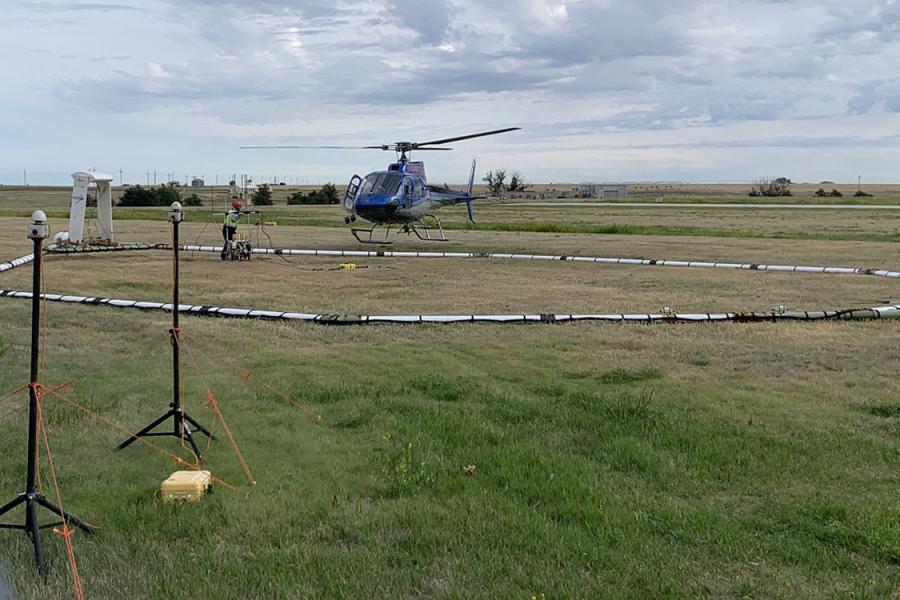 A helicopter connected to airborne electromagnetic survey instruments prepares to take off.