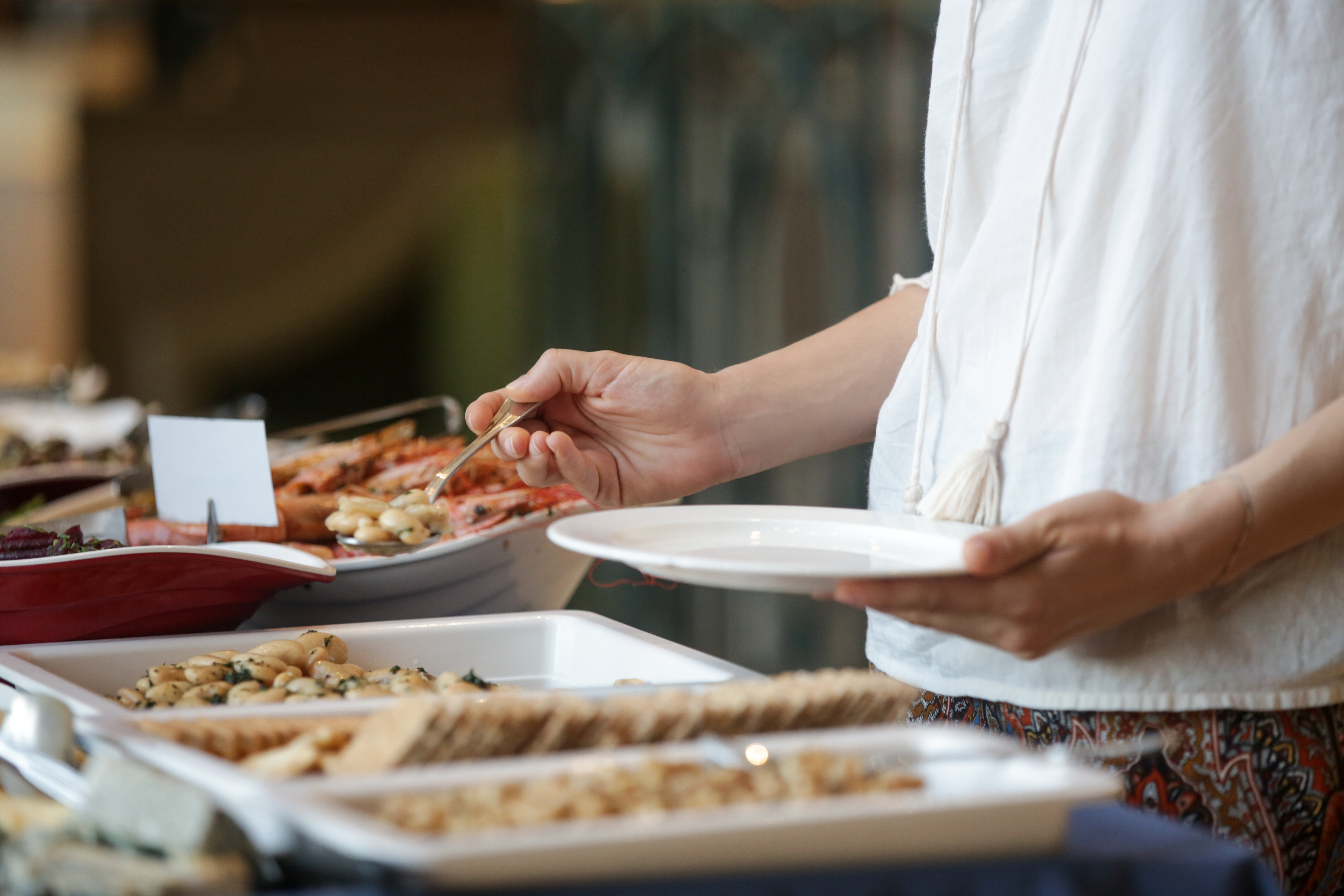 "A woman wearing a white blouse serves herself food from a buffet"