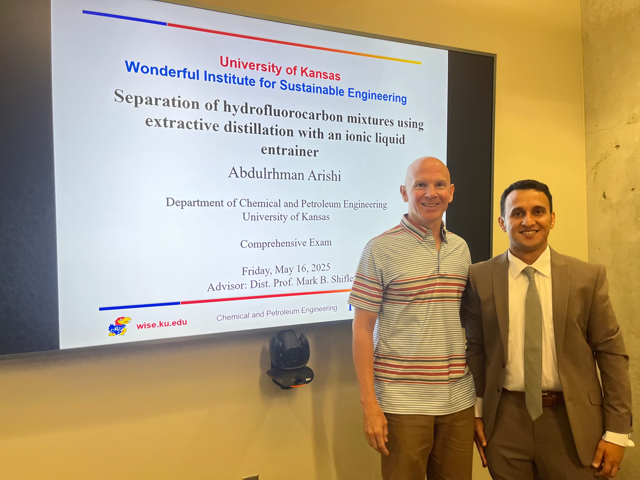 Two people posing for a photo in front of a presentation screen