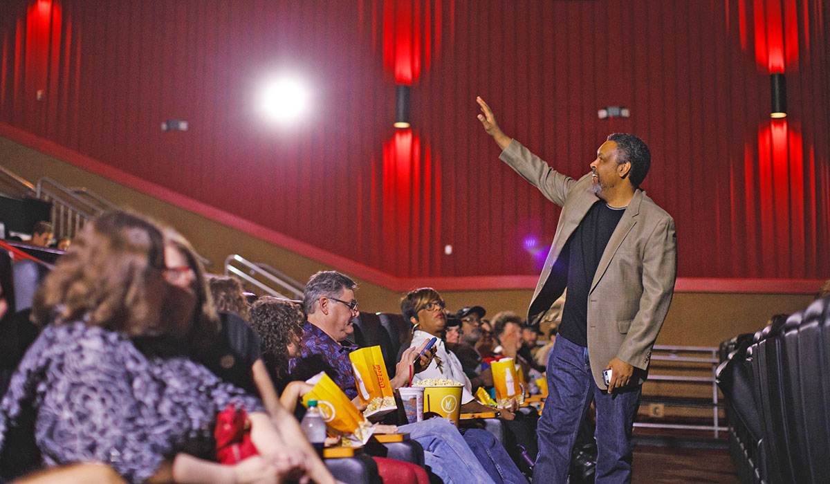 Kevin Willmott gestures to audience members seated in a theatre auditorium.