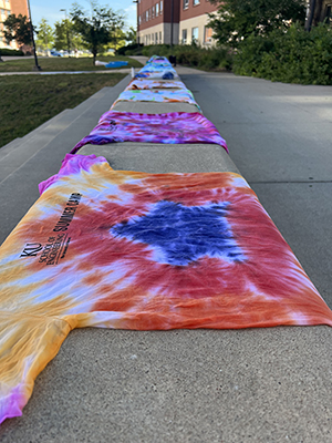 Tie-dye T-shirts set along concrete walkway with KU Summer Engineering Camp lettering.