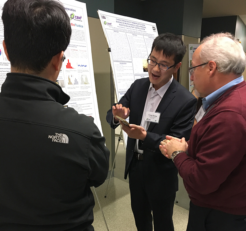 Three people standing in front of a research poster, one showing Dr. Soper something on a smartphone.