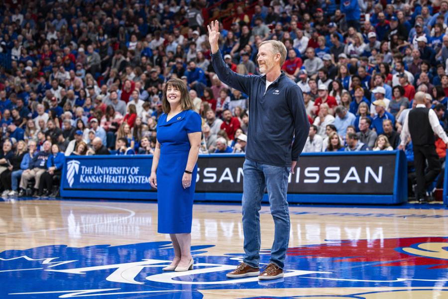 Mike Wilkins, professor of business, waves at the crowd during a KU basketball game alongside dean Paige Fields.