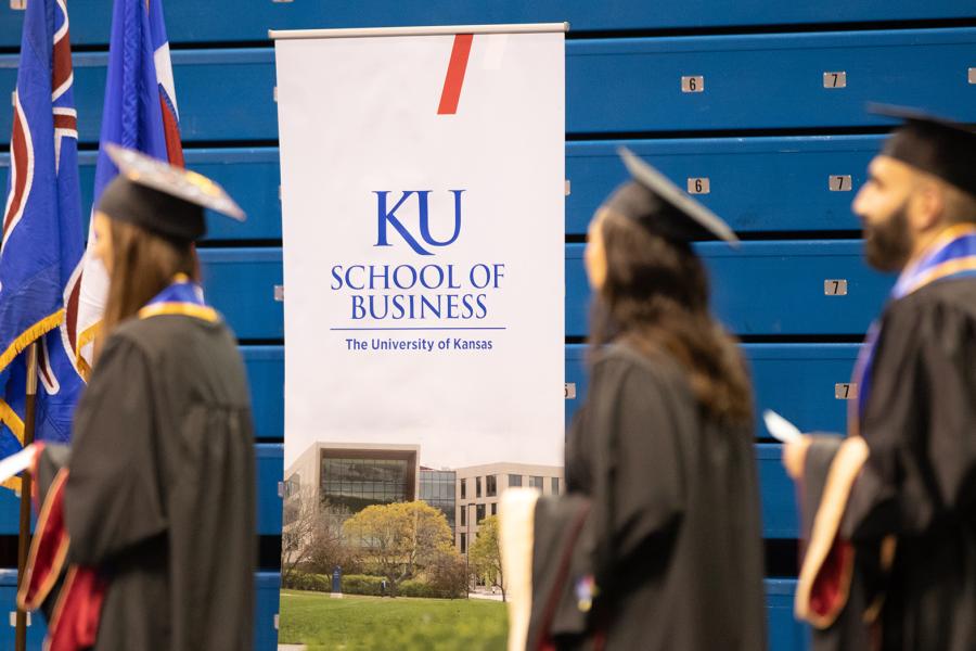 Master's graduates walk past a KU School of Business banner during a graduation ceremony in Allen Fieldhouse.