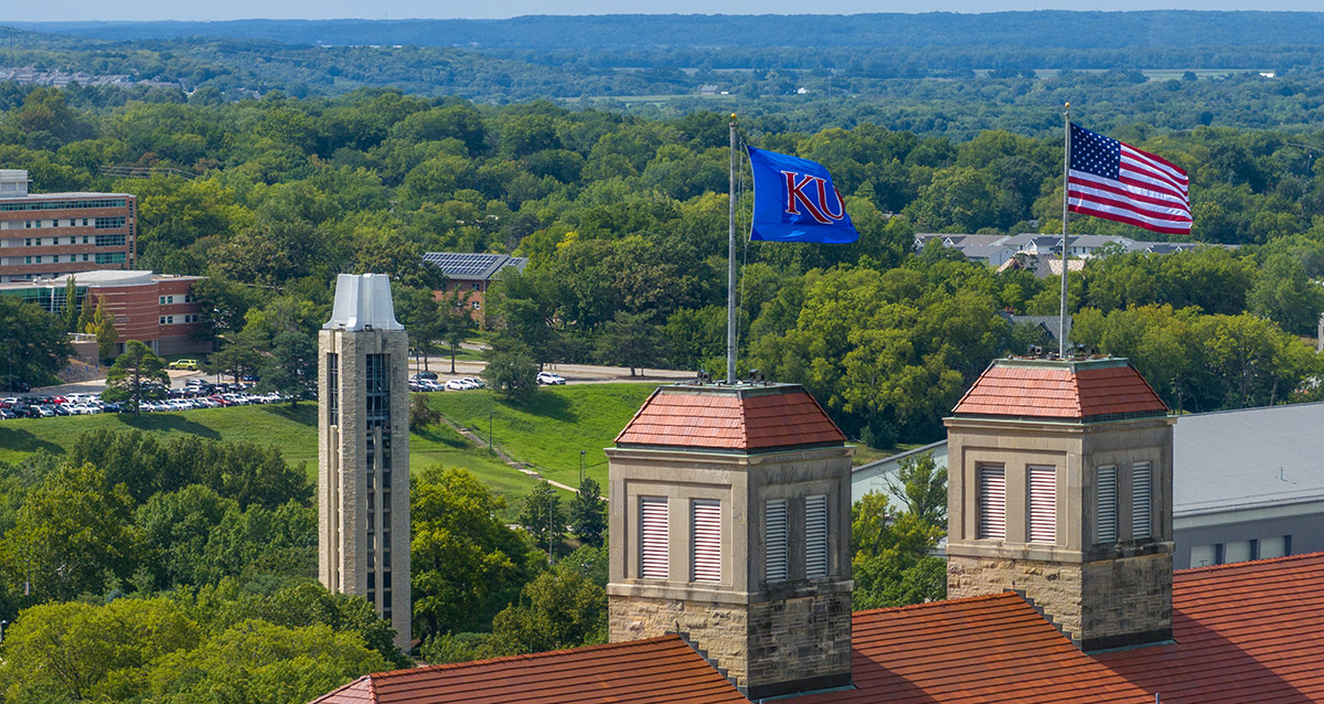 KU, American flags atop Fraser Hall with partial aerial view of Lawrence.
