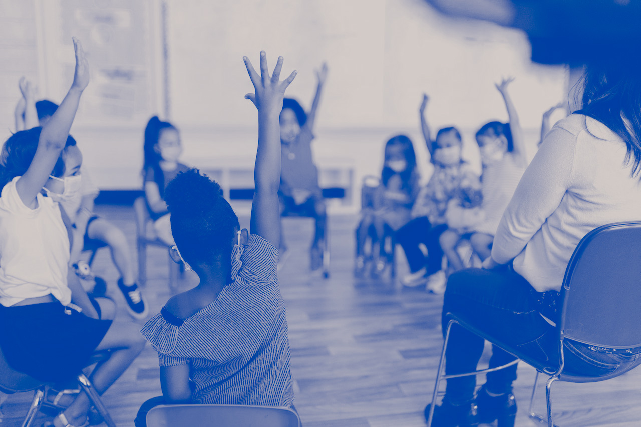 Students raise their hands to be called on in class while sitting in a circle