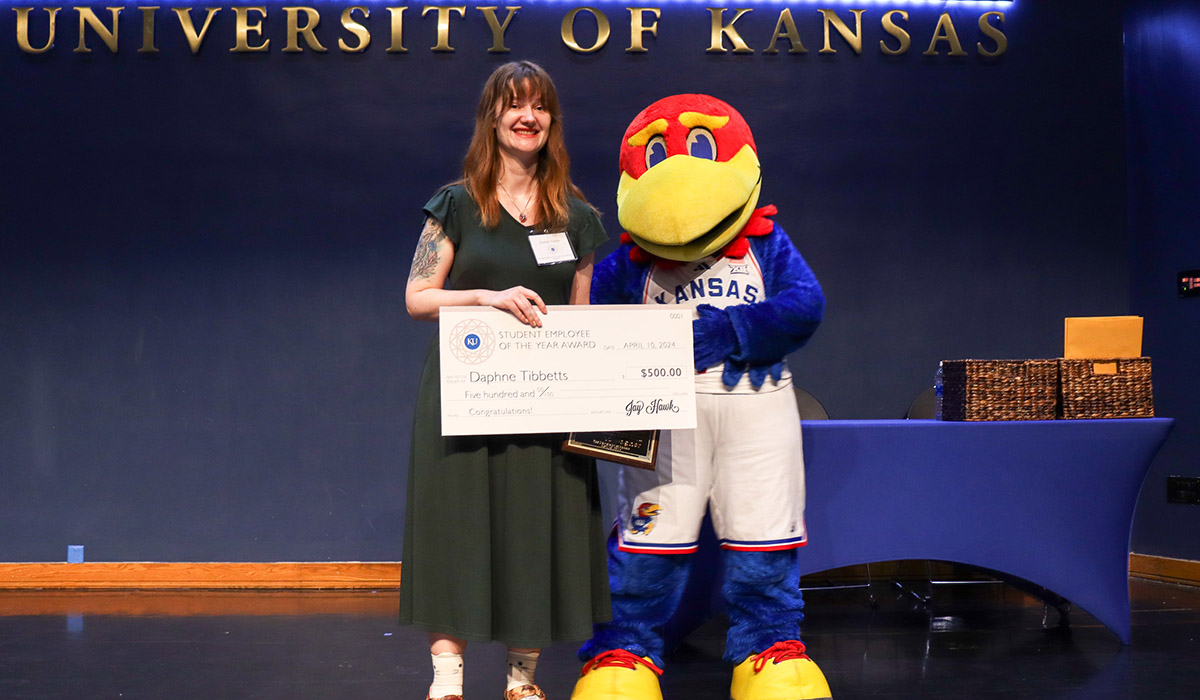 Daphne Tibbetts and Baby Jay hold a plaque on stage at the Student Employee of the Year ceremony.