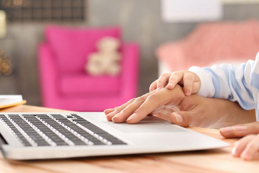 Adult guiding child's hand on laptop keyboard.