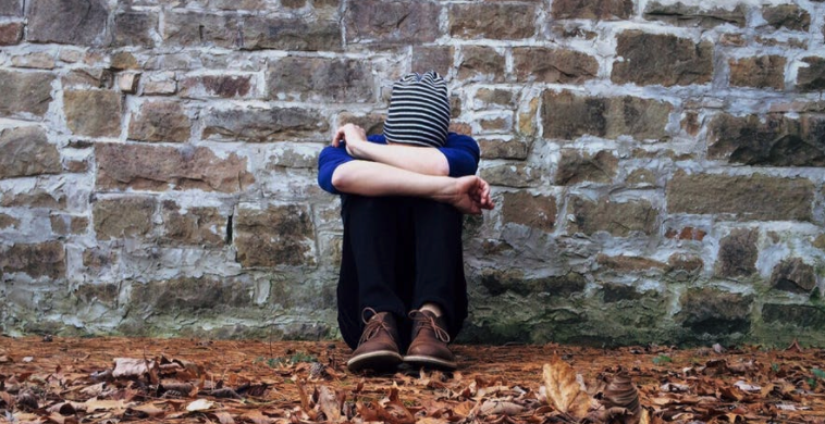 Person covers their face with their arms while sitting on the ground