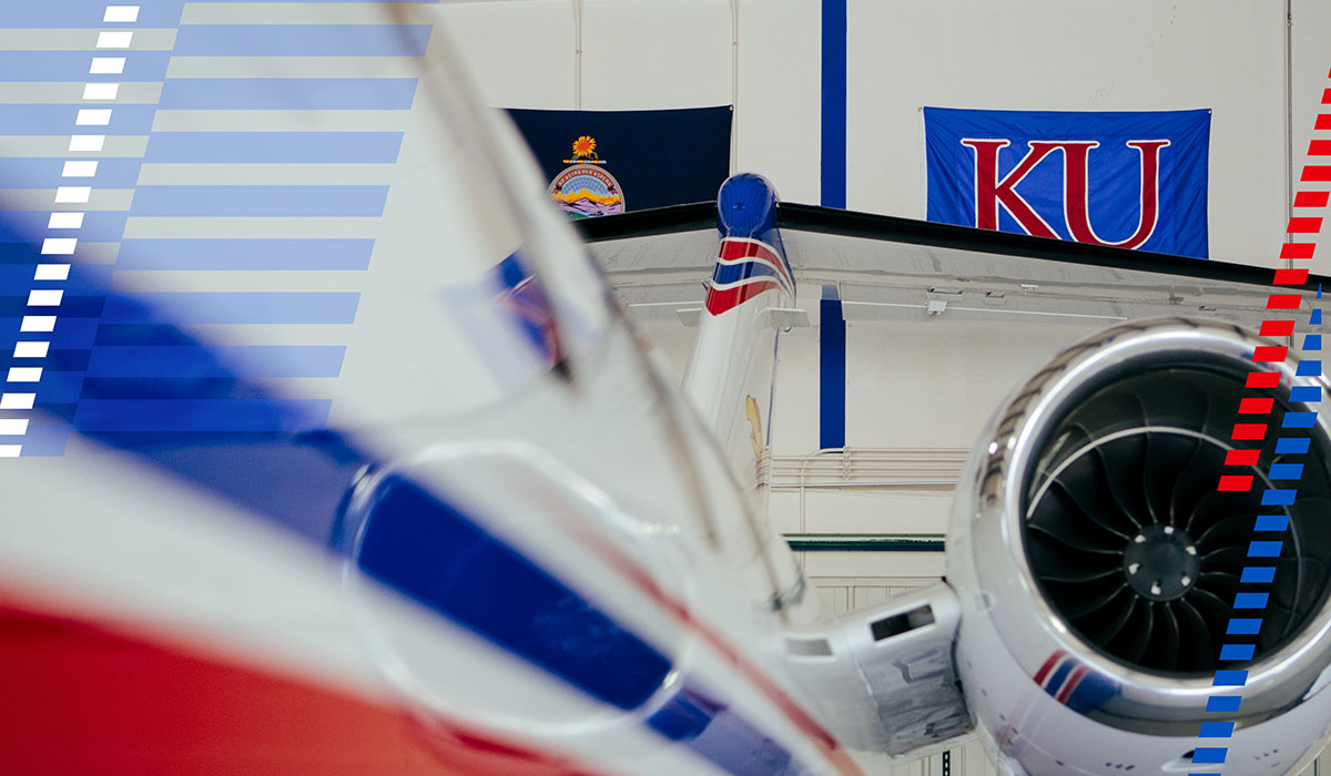 Closeup of aircraft with red and blue coloring and KU, Kansas flags in background.