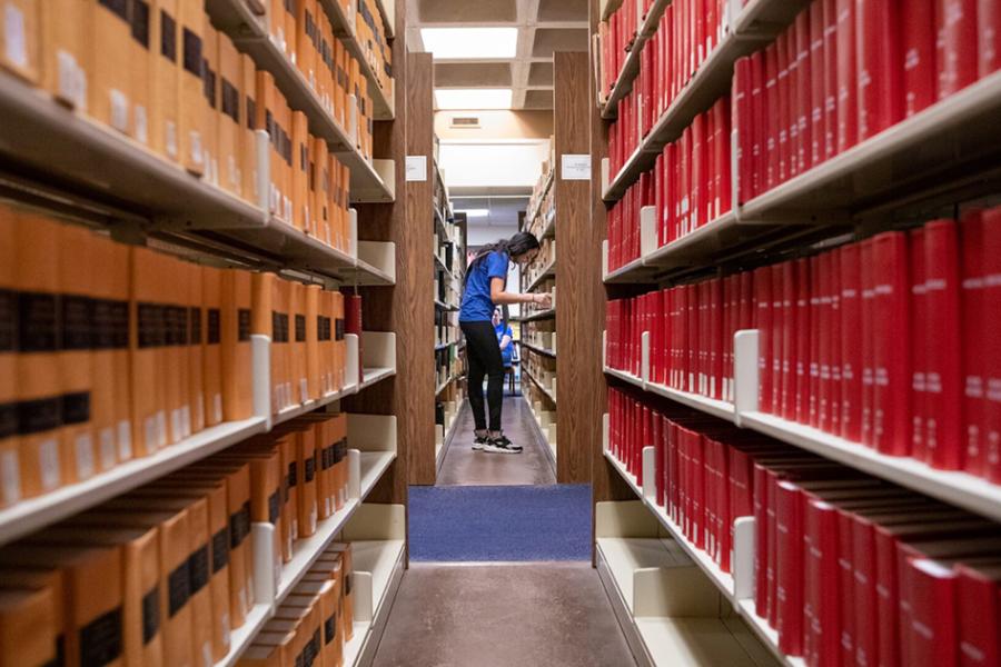 A Univeristy of Kansas School of Law student browsing through stacks of books at the law school's library.