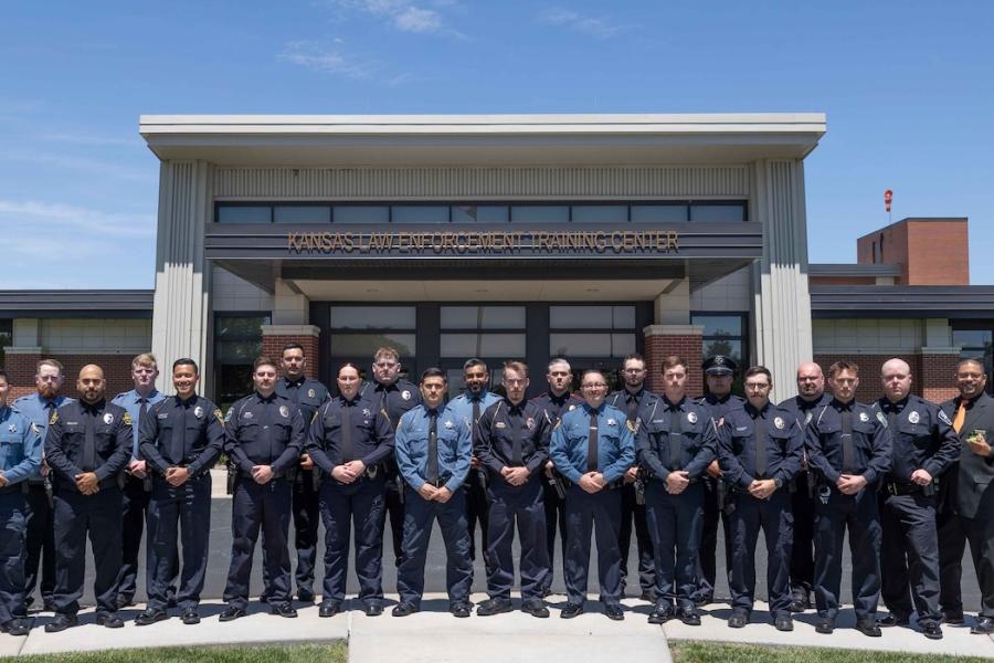 Law enforcement officers in uniform stand in front of a building on the the Kansas Law Enforcement Training Center.