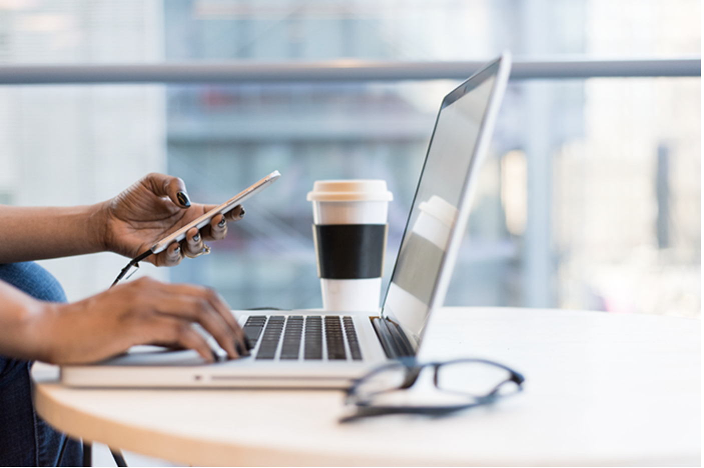 Hands typing on a laptop and checking a phone