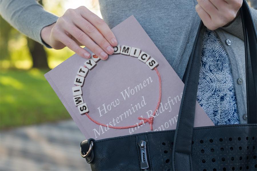 A photo of a woman's hand pulling the book "Swiftynomics" from a handbag.