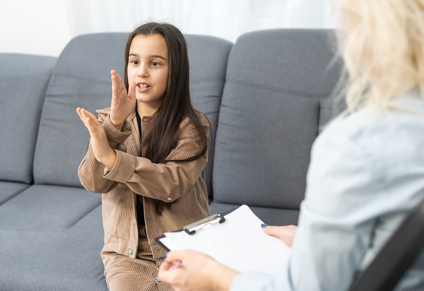 "A girl in late elementary school years uses her hands as she speaks to a woman sitting next to her"