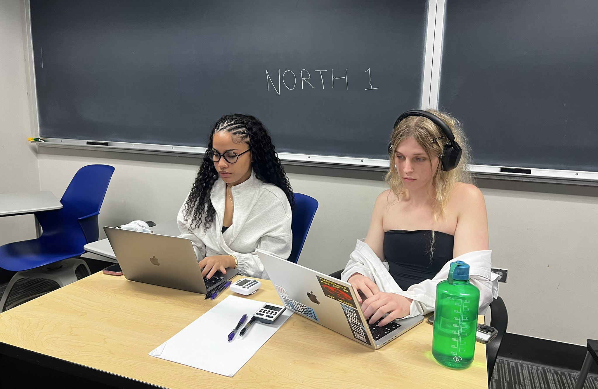 Brooklynn Hato and AJ Persinger seated and working on laptops at a debate tournament.