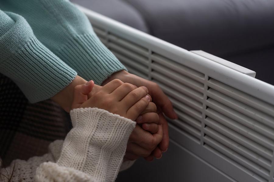 An adult and child hold hands to warm them near a heater.