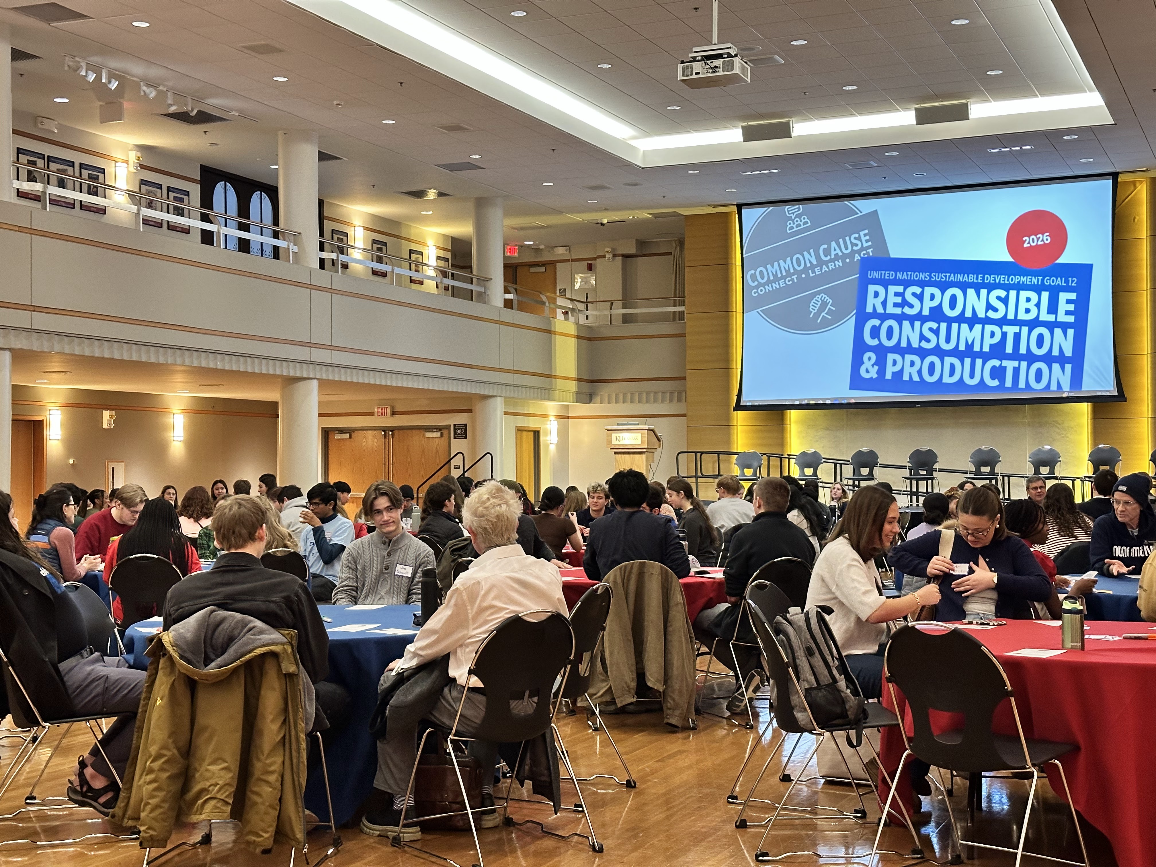 Full ballroom with people seated at round tables; screen in background says "Common Cause: Connect • Learn • Act" and "United Nations Sustainable Development Goal 12 Responsible Consumption & Production"