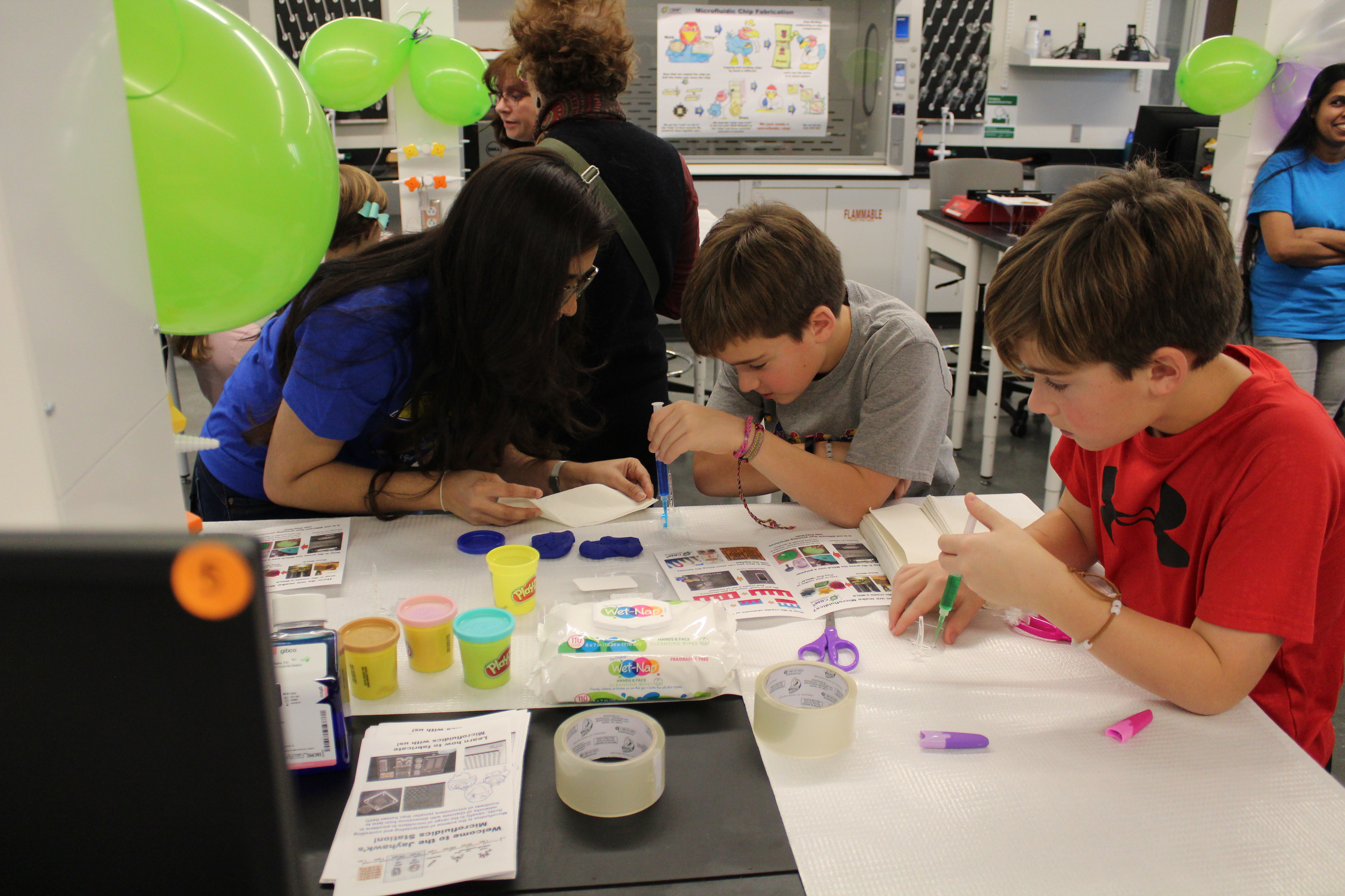 Adult providing guidance to two children while they work on a craft project.