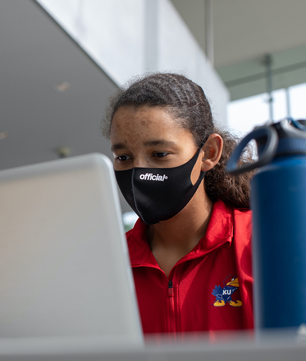 KU student working on computer, wearing face mask