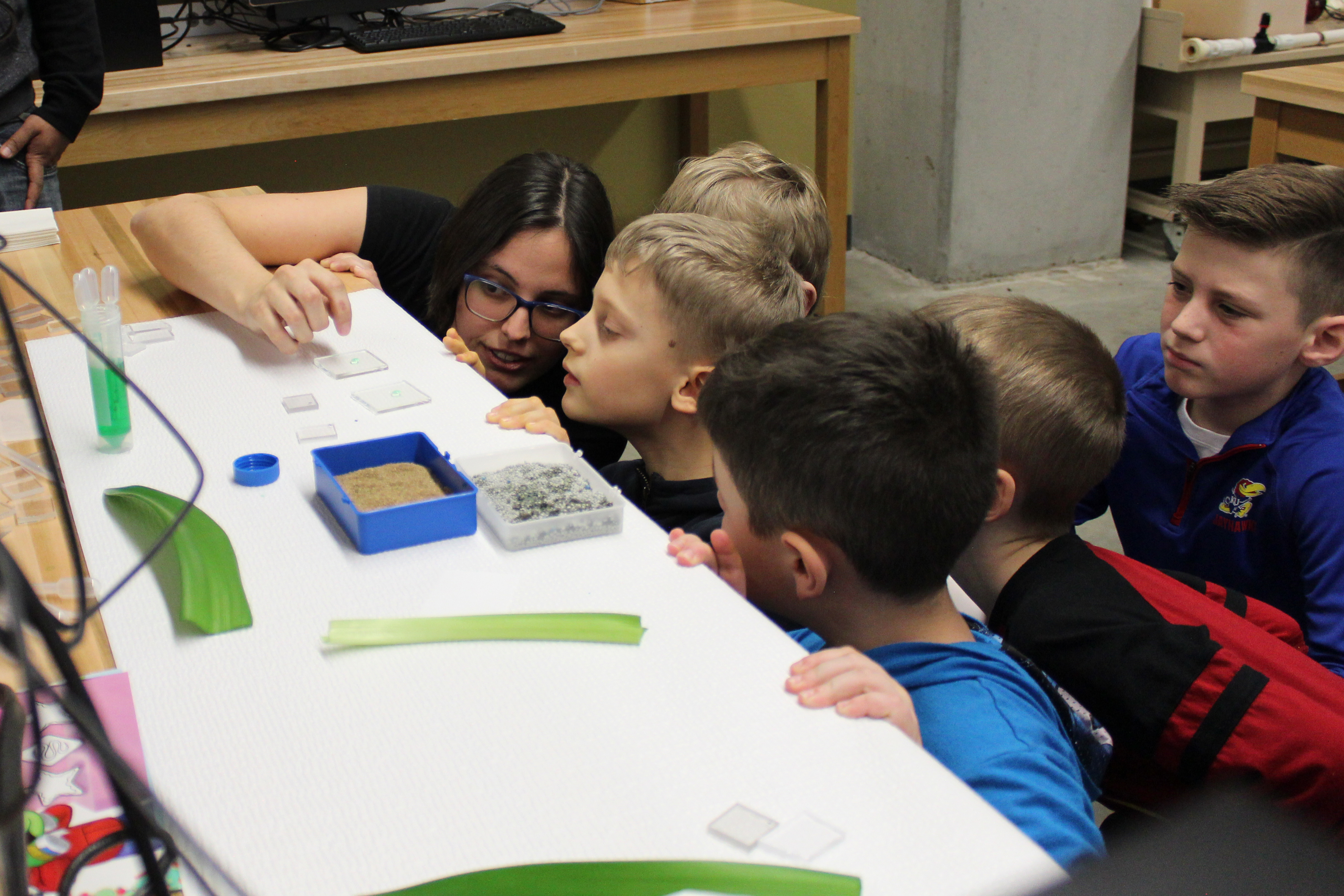 A group of students looking intently at a microscope glass.