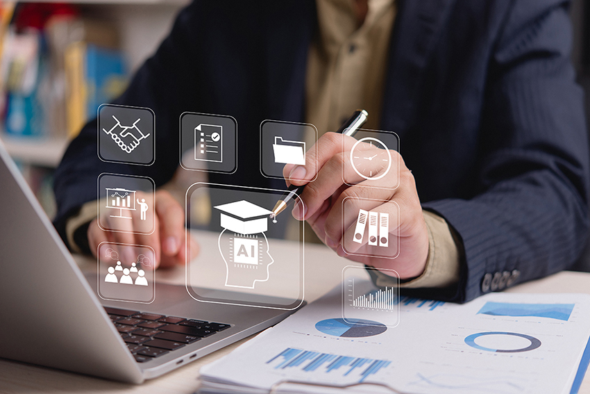 Two hands, one resting on a computer and the other holding a pen. There are icons over the image with an outline of a head with AI imprinted over it.
