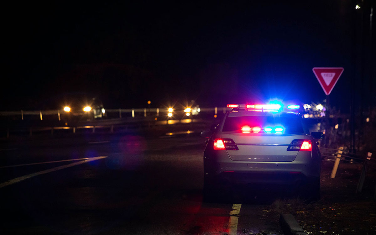 An image of police lights on a dark highway as an officer has pulled over a vehicle.