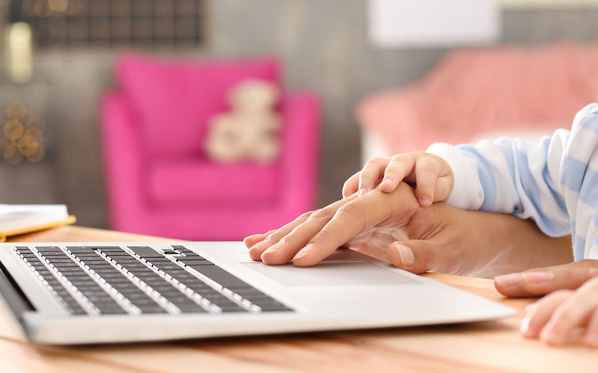 Adult guiding child's hand on laptop keyboard.