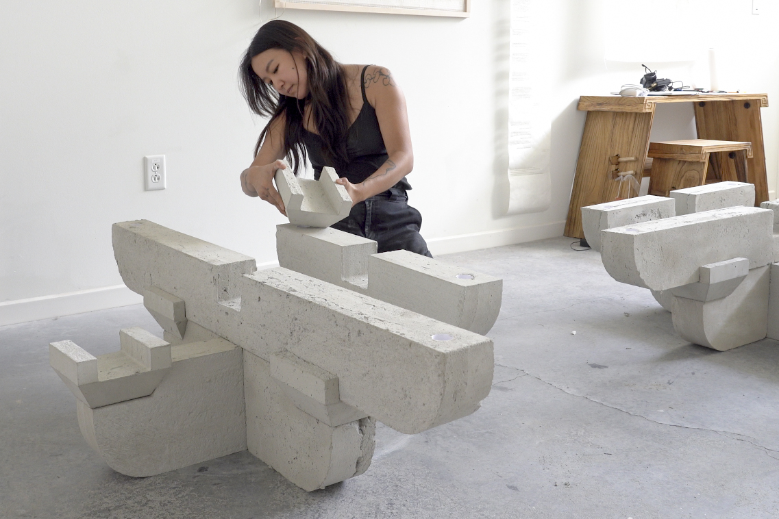 A woman with long dark hair puts together a concrete sculpture