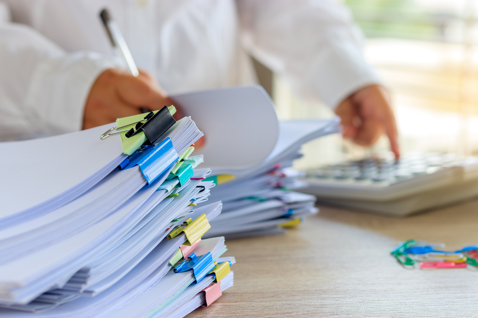 A man in a white shirt flips through stacks of papers while keying in numbers on a calculator