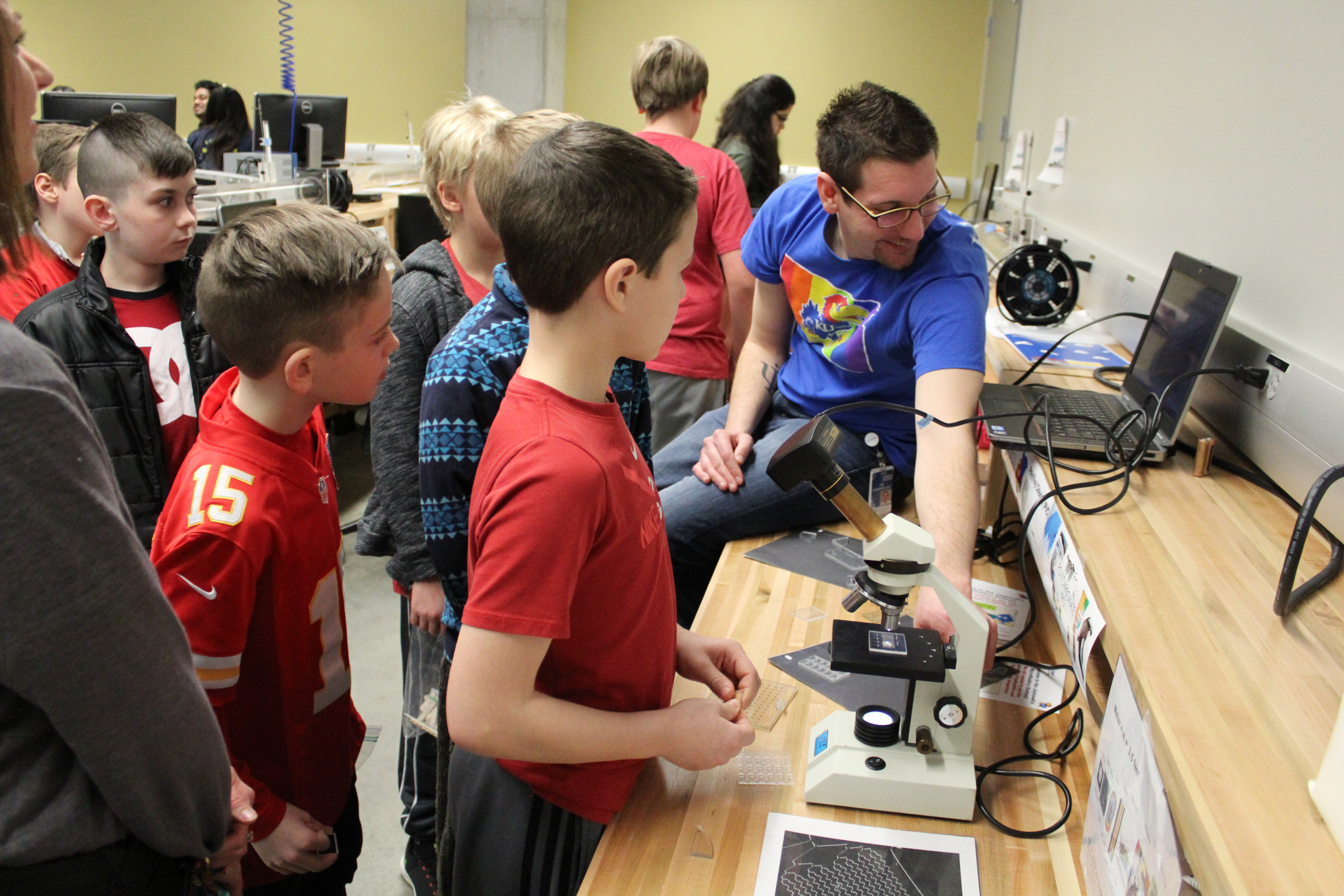 Students gathered around a helper, demonstrating something on a compter.