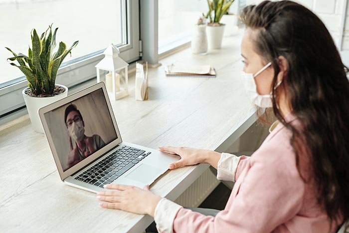 Woman with mask talking to expert on laptop