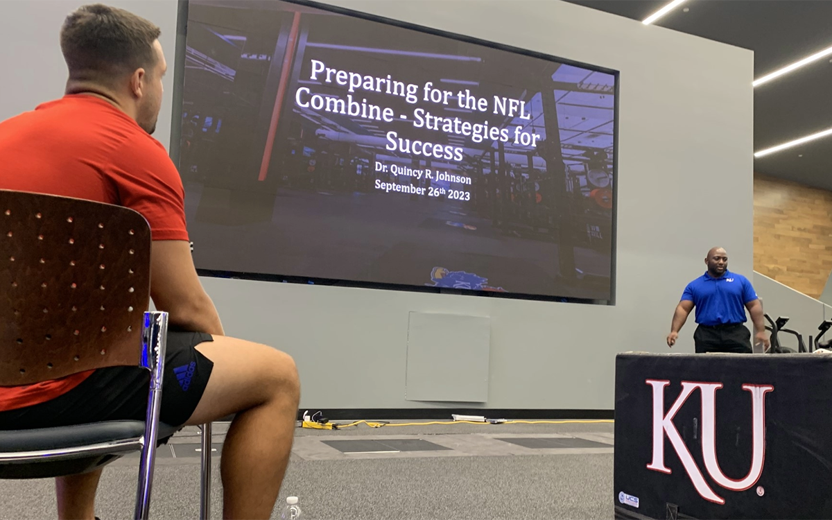 Seated individuals listen to Quincy Johnson, KU professor, standing before presentation slide reading: "Preparing for the NFL Combine: Strategies for Success."