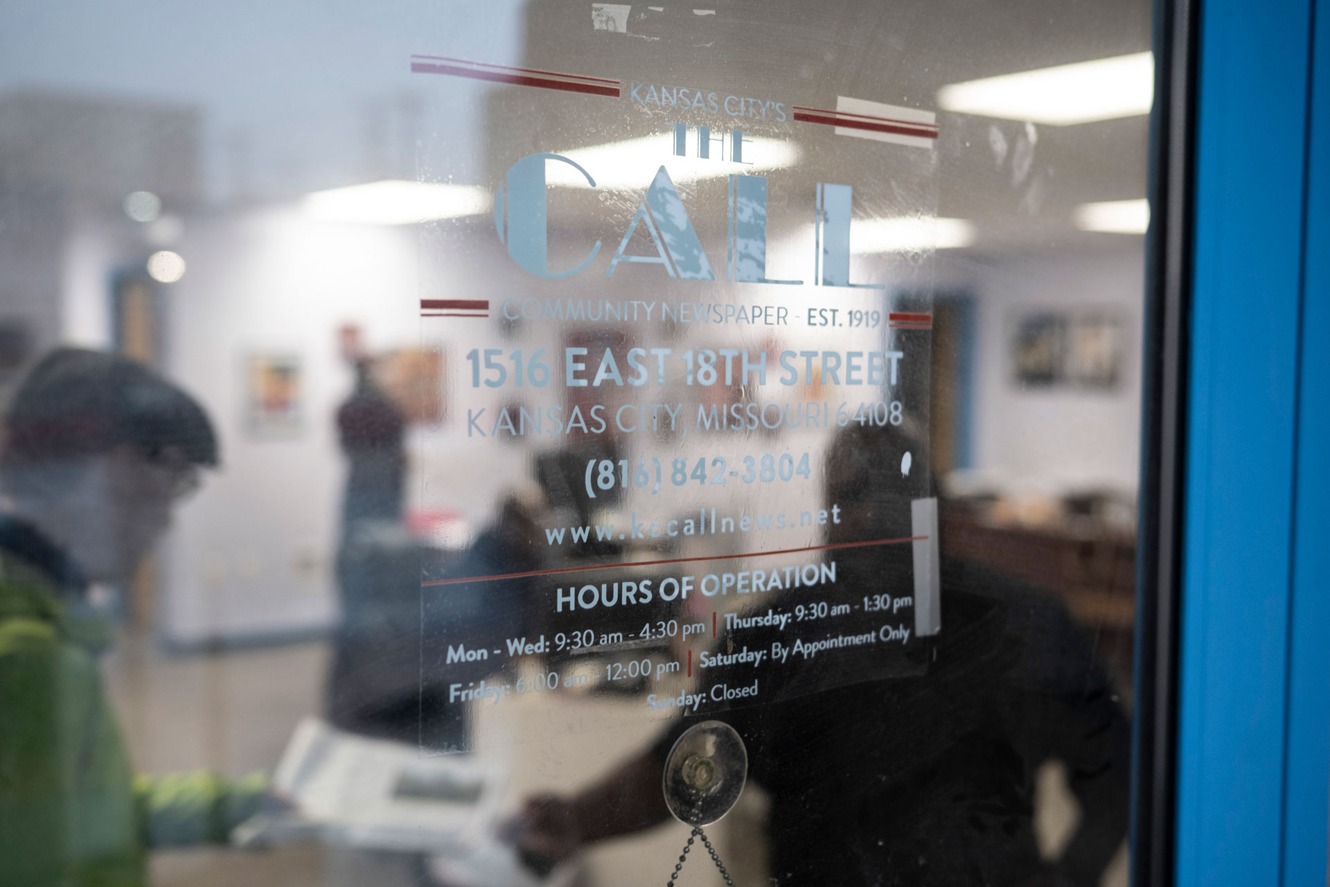 The door of Kansas City's The Call newspaper with blurred people standing behind.