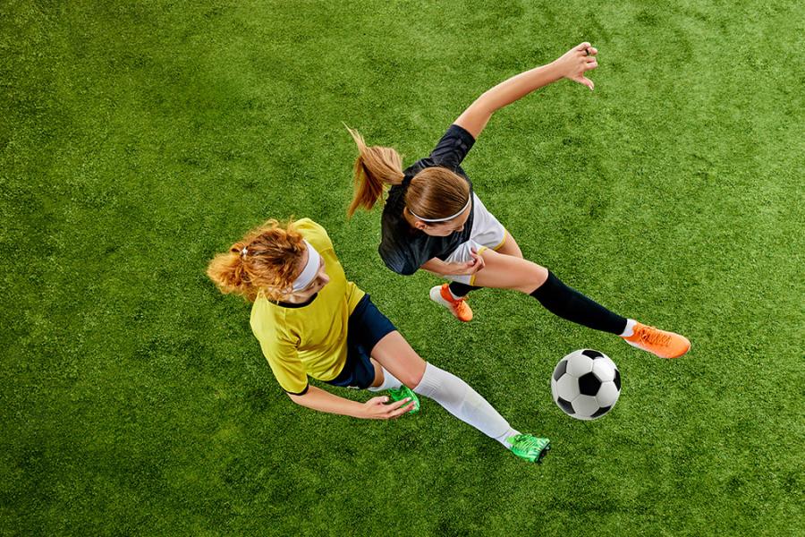 An overhead photo of two women playing soccer, both contesting for a ball.