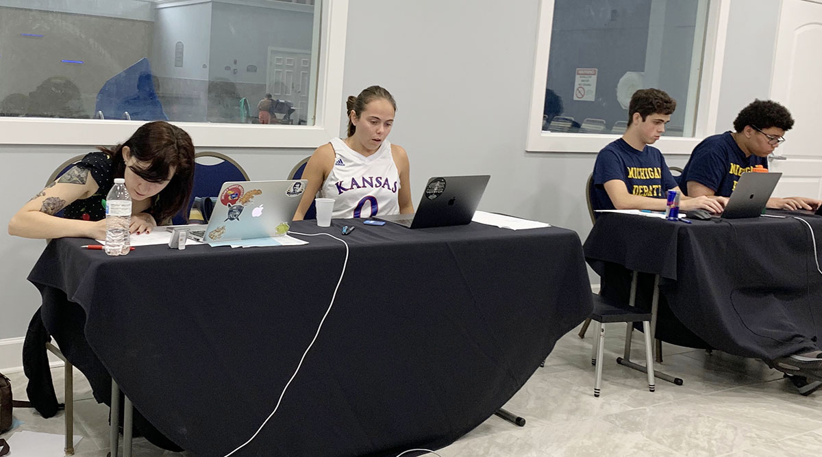 Two young women from the Kansas Debate team engage with two young men wearing University of Michigan T-shirts at a tournament.